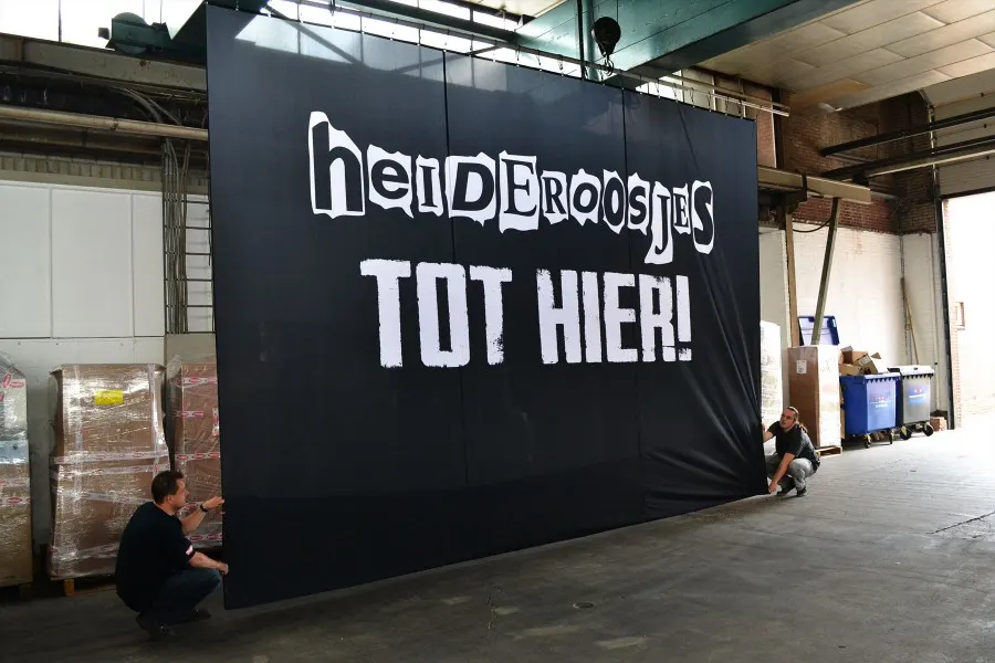 Large black Heideroosjes backdrop, “Tot hier!”, hung in a warehouse